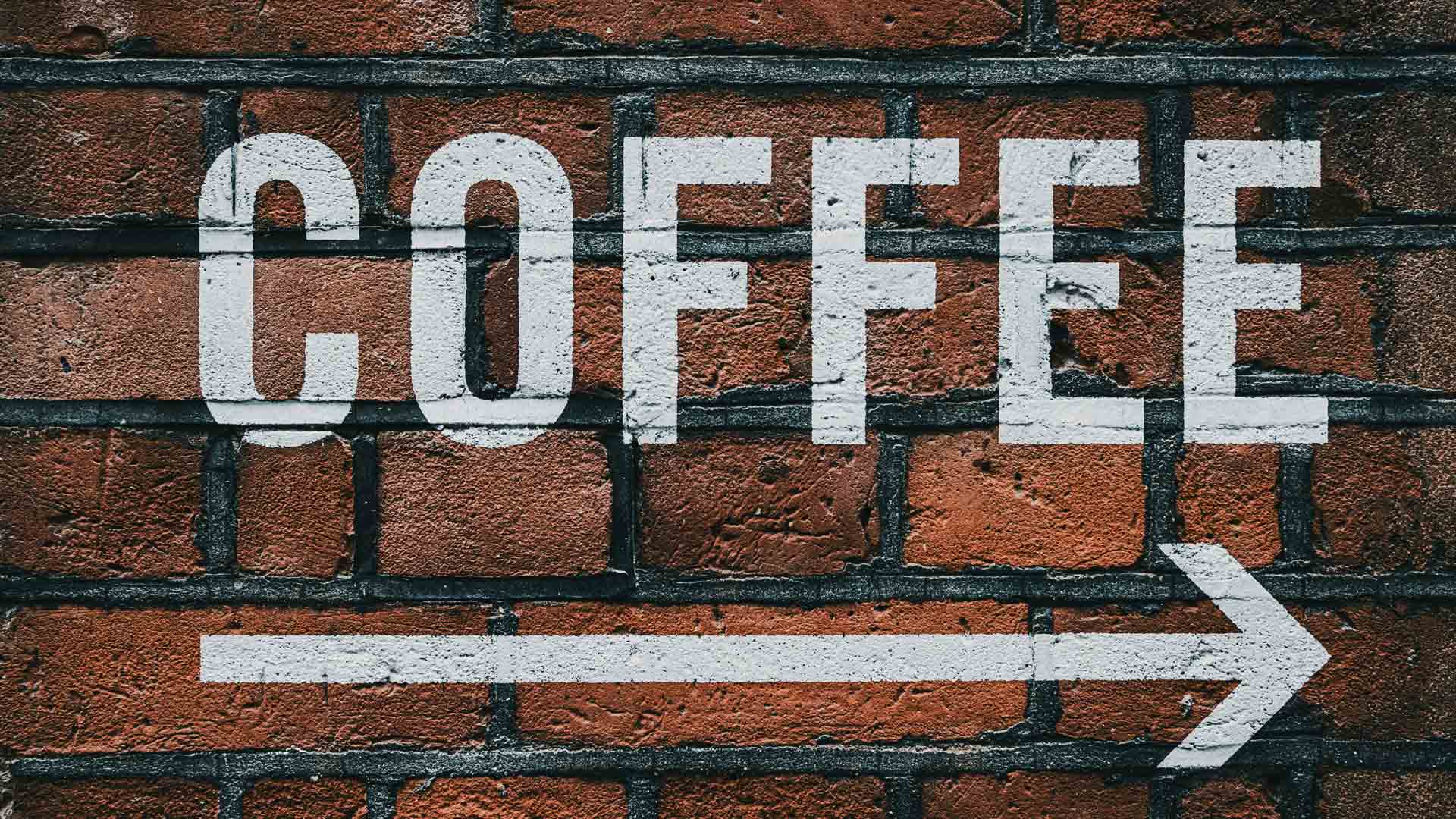 White graffiti spelling "COFFEE" on a textured brick wall, with a right-pointing arrow underneath.