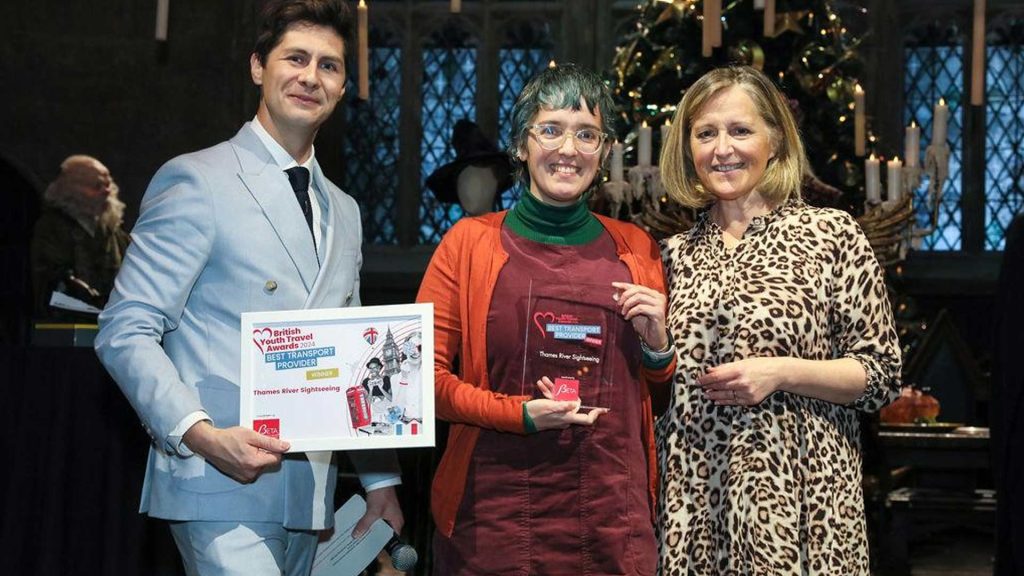 Three people stand in front of a decorated backdrop, holding awards for the British Youth Travel Awards 2023, celebrating Thames River Sightseeing.