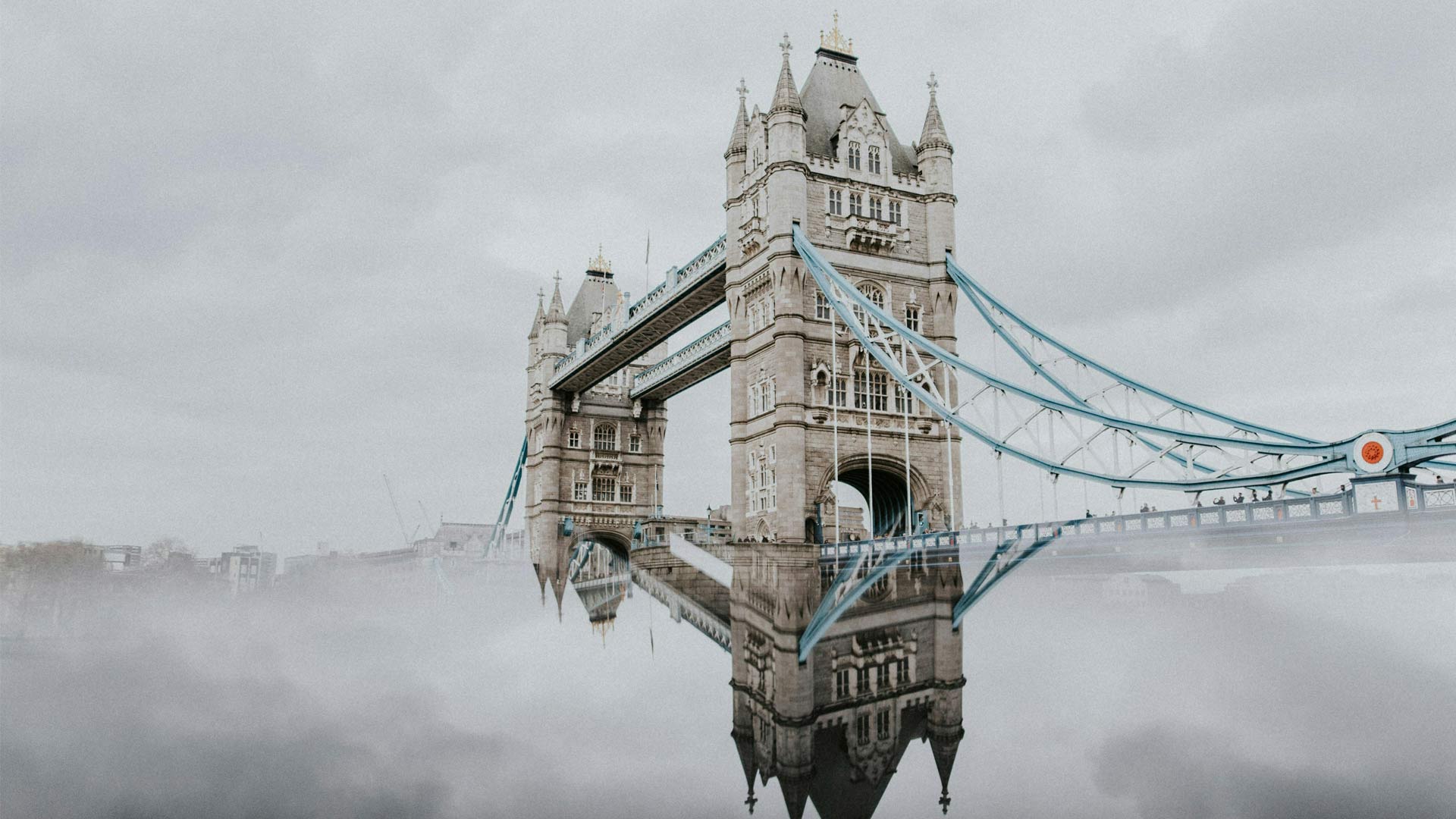 Tower Bridge in London with a reflective river surface under cloudy skies, highlighting its iconic Victorian architecture.