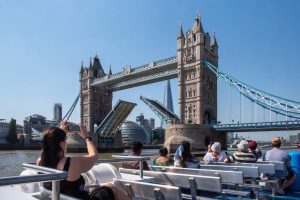 Passengers on a Thames River Sightseeing cruise photographing the iconic Tower Bridge opening in London.