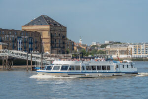 Sightseeing boat on a Thames River cruise passing historic buildings and piers on a sunny day in London.