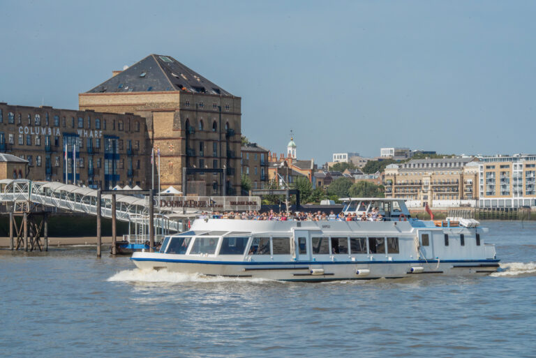 Sightseeing boat on a Thames River cruise passing historic buildings and piers on a sunny day in London.