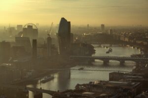 An aerial photograph of the River Thames at sunset, showing the iconic London cityscape shrouded in fog.